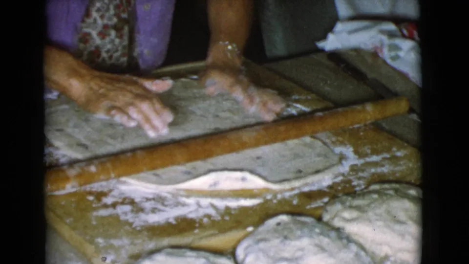 Hands adjust and smooth a thin sheet of dough on a floured wooden board, with a rolling pin nearby in the 1968 Cottonwood footage.