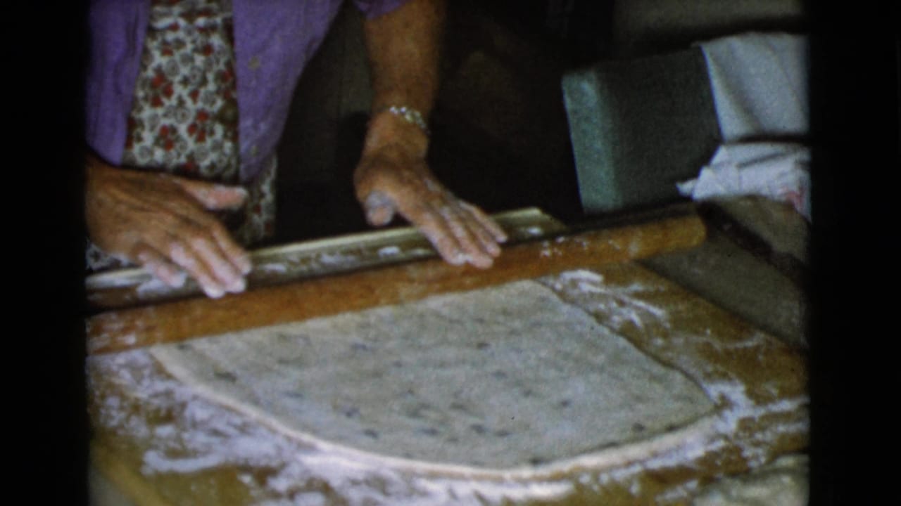 Woman's hands press a rolling pin over dough on a floured wooden surface.