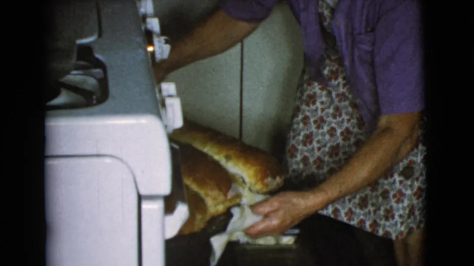 The woman steadies golden loaves near the vintage oven in the Cottonwood, Arizona 1968 home-movie kitchen scene.