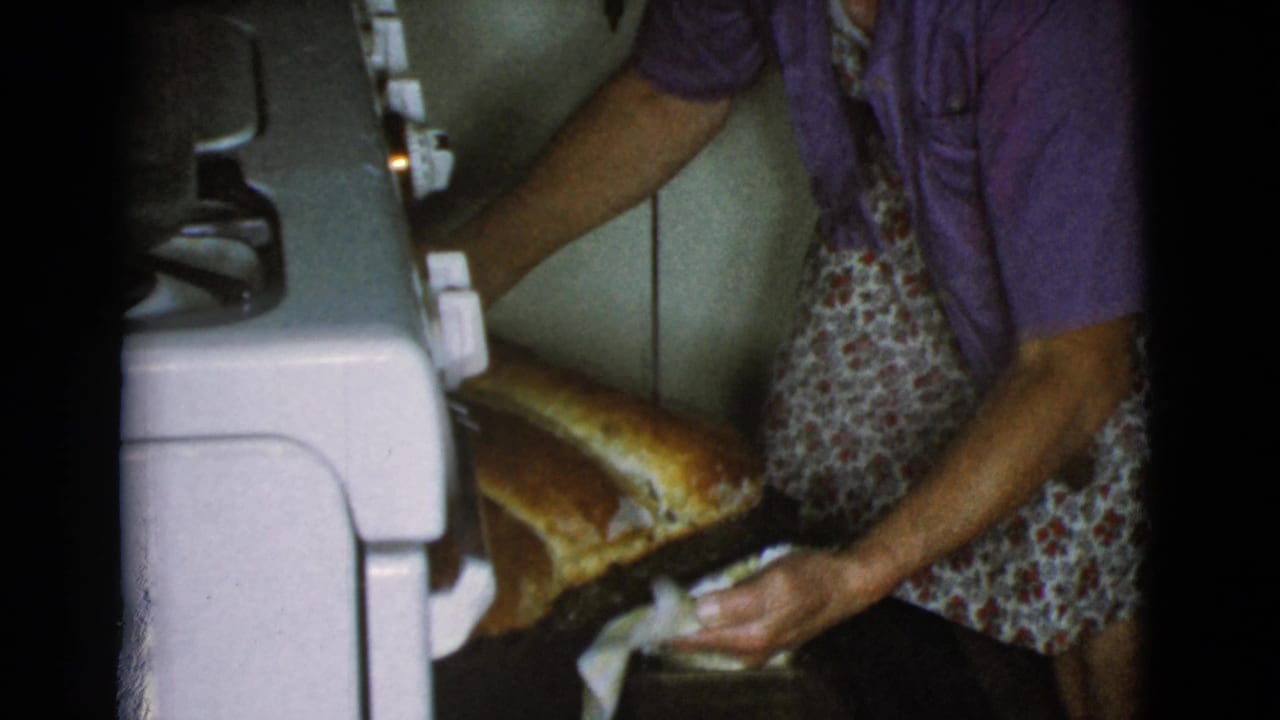 Woman in apron removing large bread loaves from a white oven.