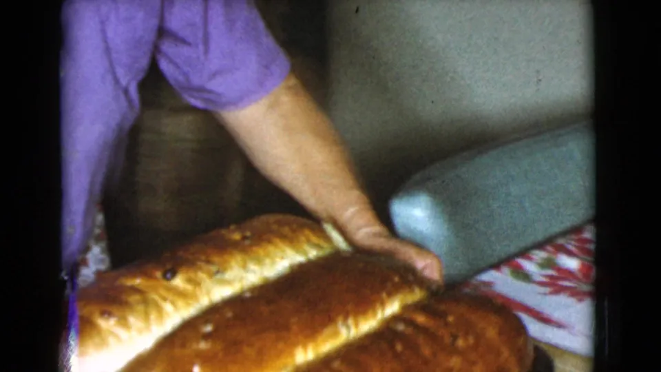 A close 8mm frame shows the woman's hands steadying large baked loaves on a tray in the Cottonwood, Arizona kitchen.