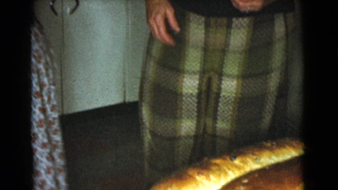 Adult woman in a plaid skirt stands beside long bread loaves on a kitchen counter.
