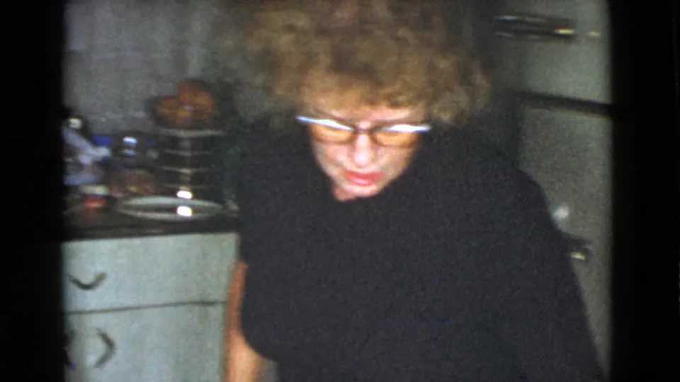 An adult woman with glasses and curly hair appears in front of cabinets and cookware in a 1968 Cottonwood home kitchen.