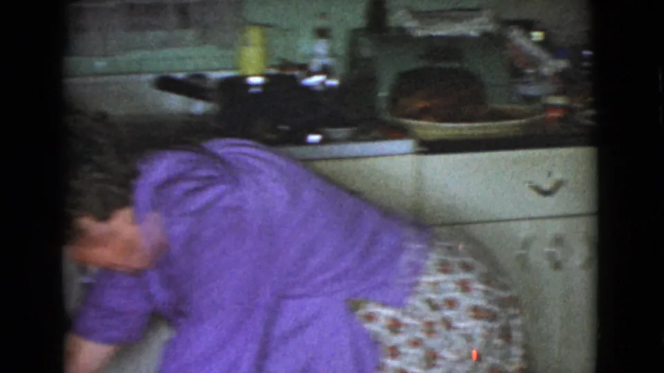 An adult woman in a purple top and floral skirt bends over the sink area in the Cottonwood, Arizona home kitchen.