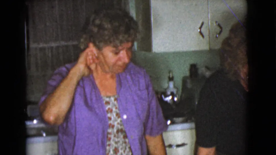 In the Cottonwood kitchen scene, the woman touches her ear as another adult figure appears at the right edge near the sink.