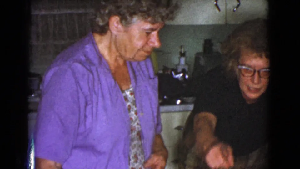 The final frame shows the woman in purple beside another adult in dark clothing who gestures toward the lower edge of the kitchen scene.