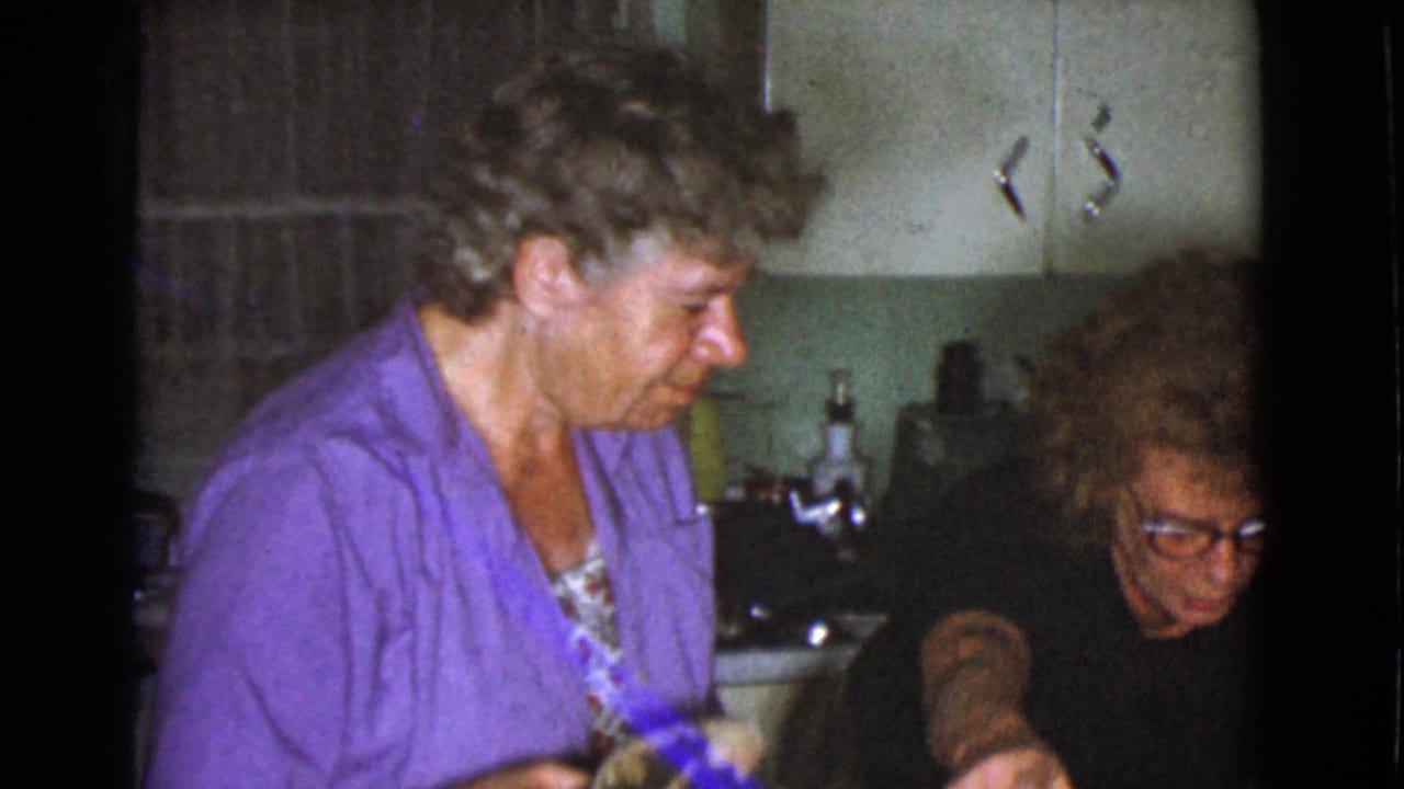 Two women seated or standing close together in a small kitchen interior.