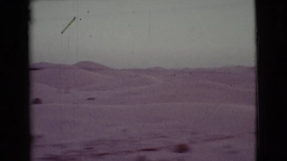 1968 Cottonwood, Arizona home-movie frame with rolling desert hills, pale sky, and scattered foreground shrubs viewed from the road.