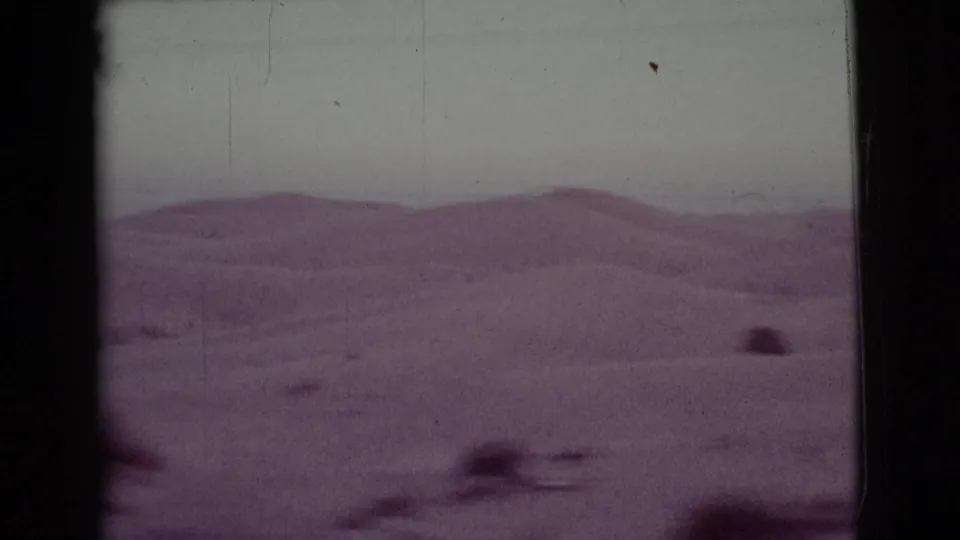 1968 Arizona 8mm frame showing low desert dunes, sparse scrub, and a hazy sky with visible film grain and gate edges.