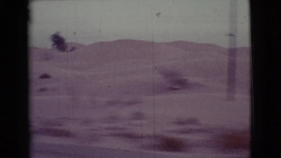 1968 Arizona 8mm frame with rolling desert terrain, scattered scrub, and a lone distant tree under a pale sky.