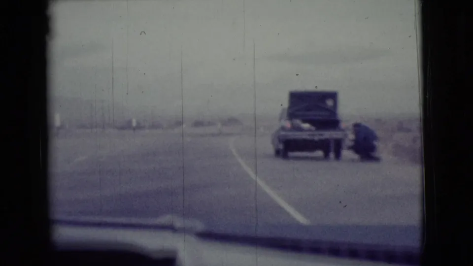1968 Arizona 8mm frame showing a sedan near the highway shoulder, its trunk open, with desert road and dashboard edge visible.