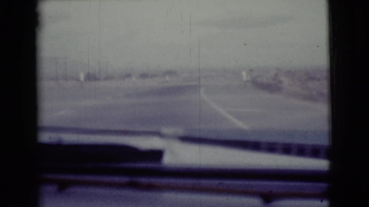 View through a car windshield toward a hazy highway in an arid landscape.