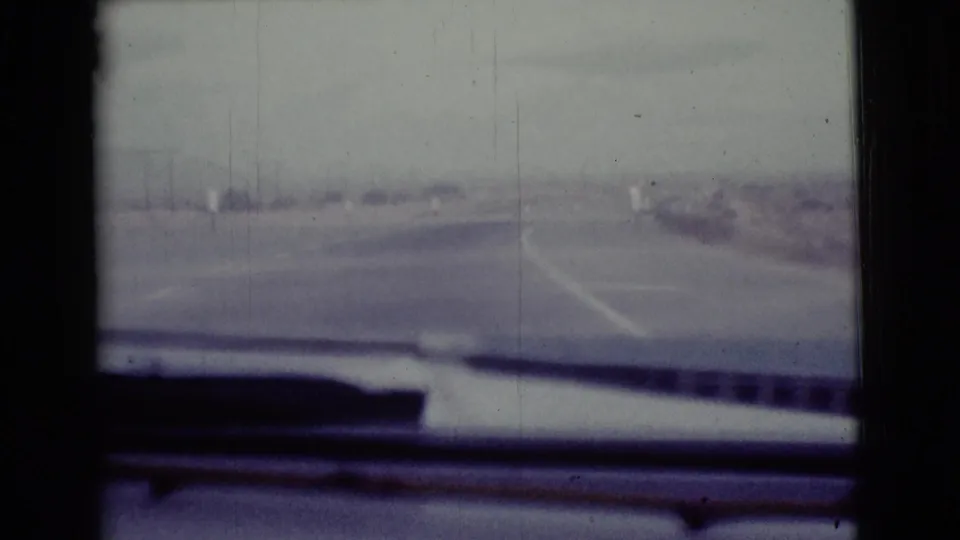 1968 8mm road-trip view near Cottonwood, Arizona, looking past the car dashboard toward a hazy two-lane highway.