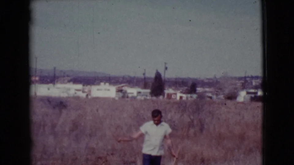 The man appears to work or reposition a shovel in the dry grass, with Cottonwood-area houses and utility poles in the distance.