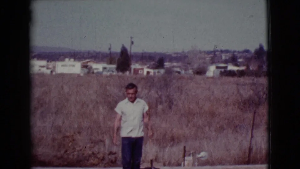A man stands by a patch of disturbed soil in a dry Cottonwood field, with a shovel and sparse suburban background visible.