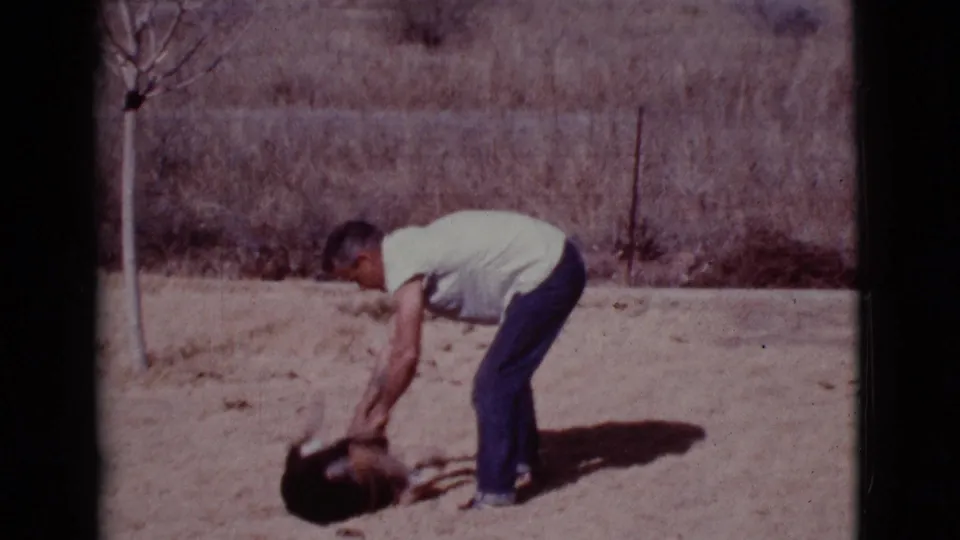 In Cottonwood, Arizona, 1968, a man in a white T-shirt bends toward a small dog on dry ground.