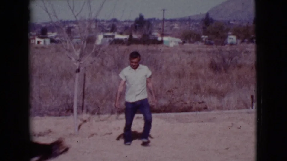 A young man in a white shirt and jeans stands in the Cottonwood yard while the German Shepherd passes quickly at the bottom of frame.