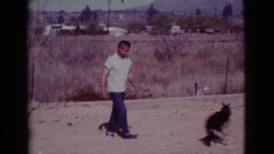 In Cottonwood, Arizona, 1968, a man walks through a dry open field as a dark dog runs ahead of him.