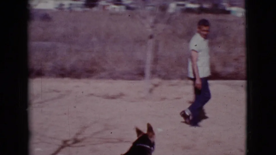 The man walks across the dry Cottonwood field as the dog's head appears at the lower edge of the 8mm frame.