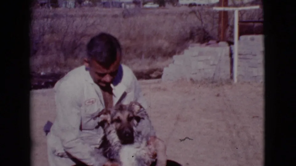 The man looks down and scrubs the dog, with dry brush and a low wall behind them in Cottonwood, Arizona.