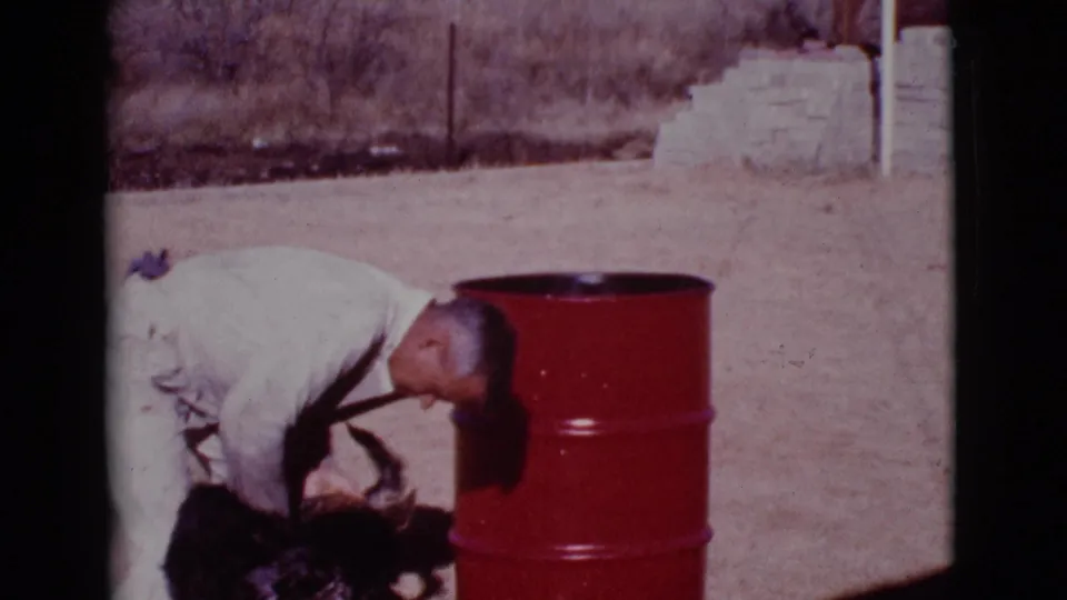 At the end of the clip, the man remains bent over the German Shepherd beside the red metal drum in the dry Arizona yard.