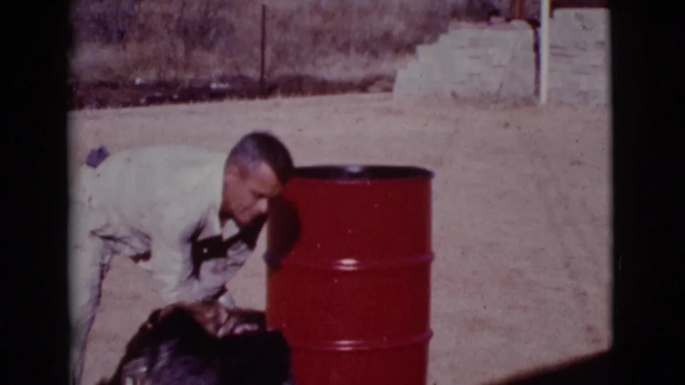 At the end of the clip, the man remains bent over the dark-furred dog beside the red barrel in the 1968 Cottonwood yard.