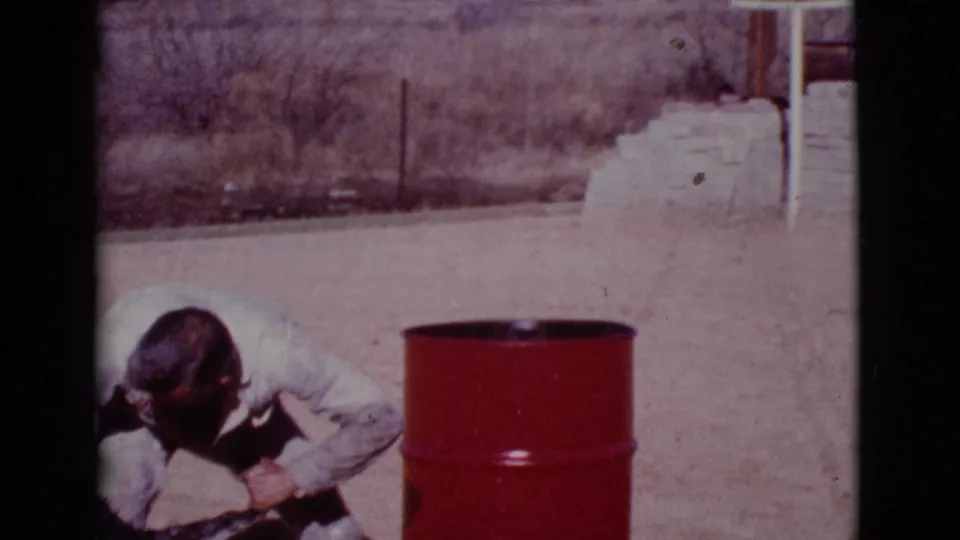 The Cottonwood, Arizona 8mm frame shows the uniformed man bent low, attending to the black dog near the red barrel.