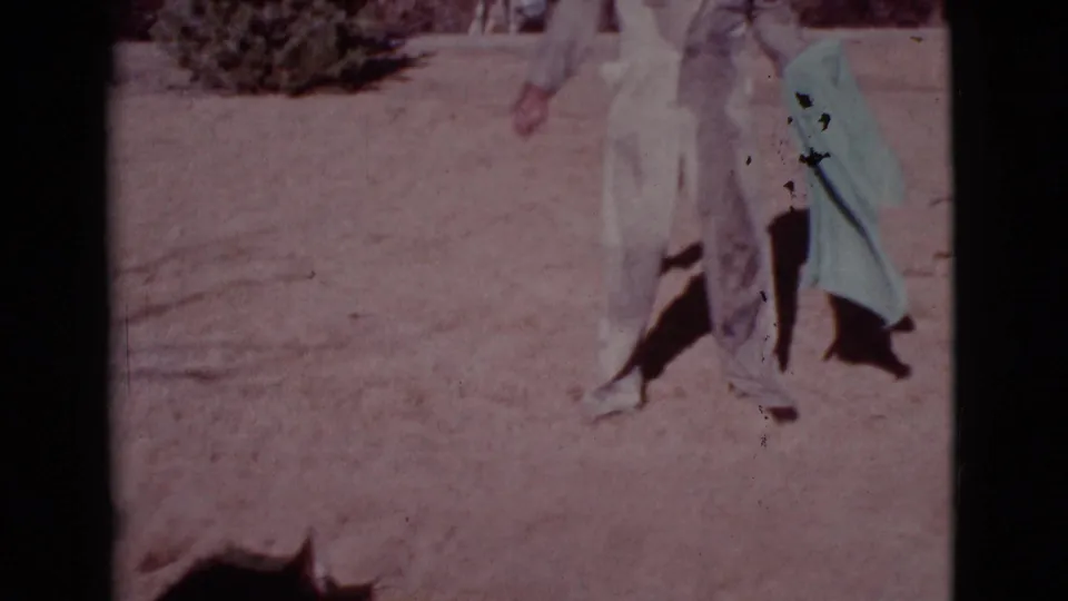 The man in light coveralls holds a pale blue towel in the Cottonwood yard while the dog is partly visible near the bottom of the frame.