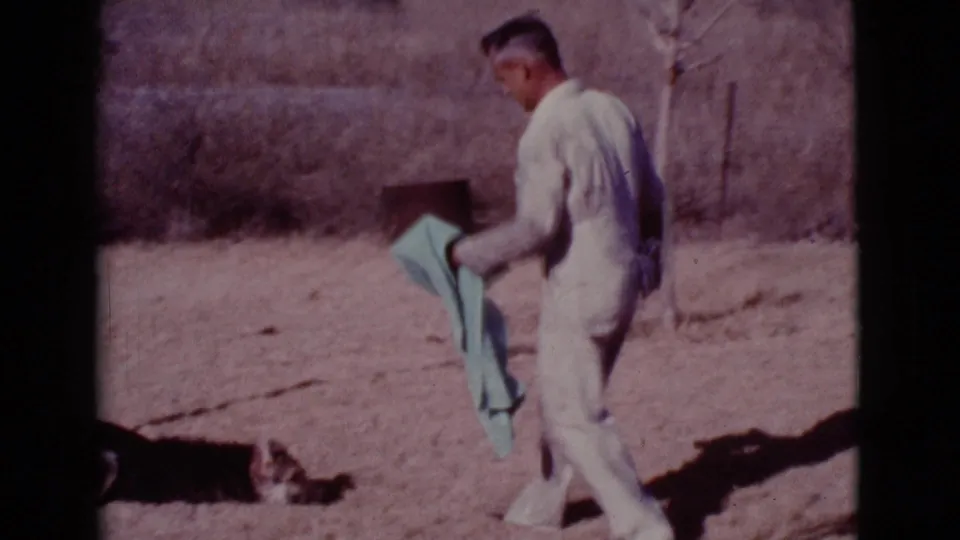 At the end of the Cottonwood home-movie clip, the man holds the towel while the dog remains low near the left edge of the dry yard.