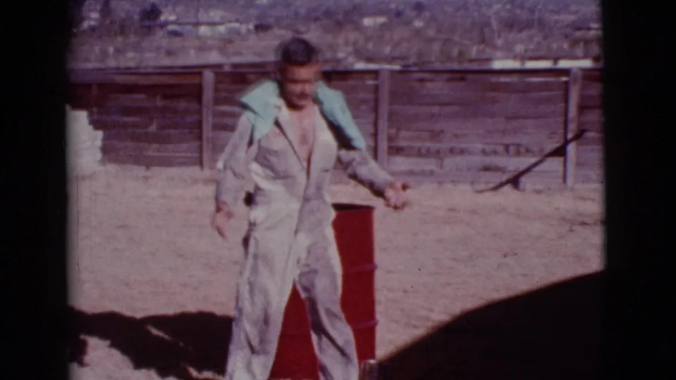 A man in a white jumpsuit and light blue collar stands next to a red barrel in a sunny Cottonwood, Arizona yard.
