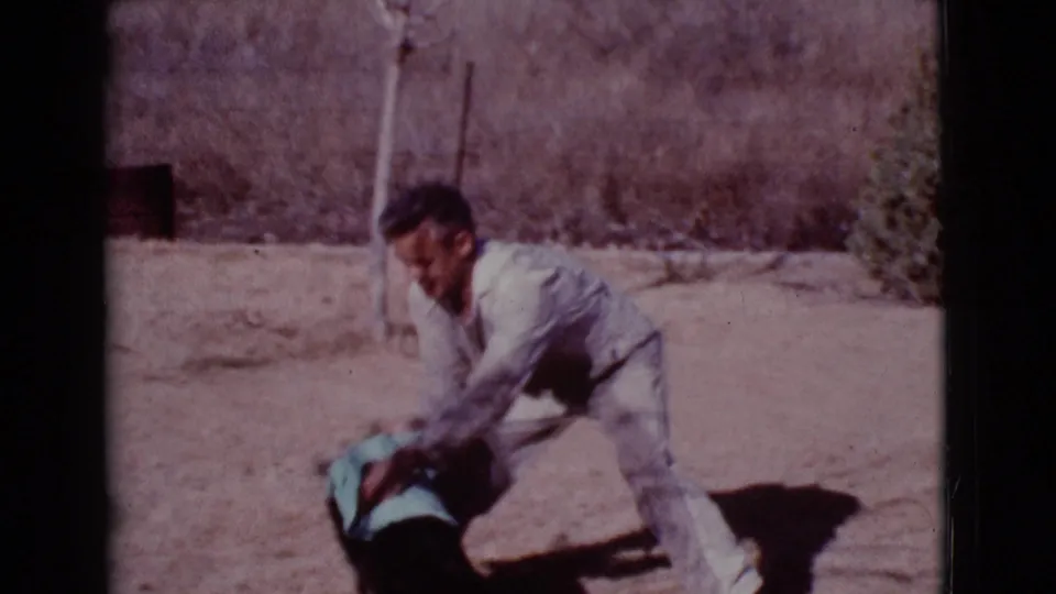 The man looks up while rubbing the black dog with a blue towel in the Cottonwood, Arizona backyard scene from 1968.