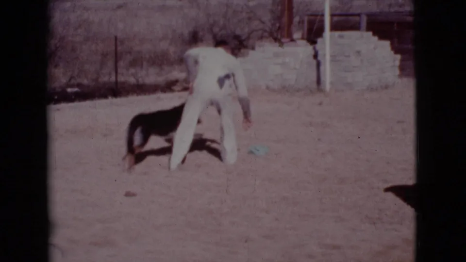 In supplied 1968 Cottonwood, Arizona home-movie footage, a man in white bends toward a German Shepherd in a dry yard.