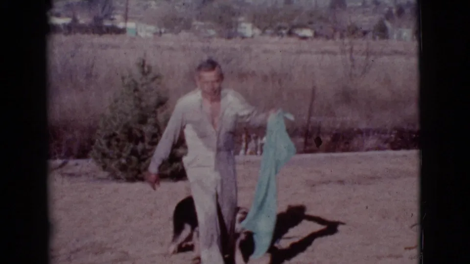 A man in white holds the teal towel beside the dog in the dry Cottonwood, Arizona backyard.