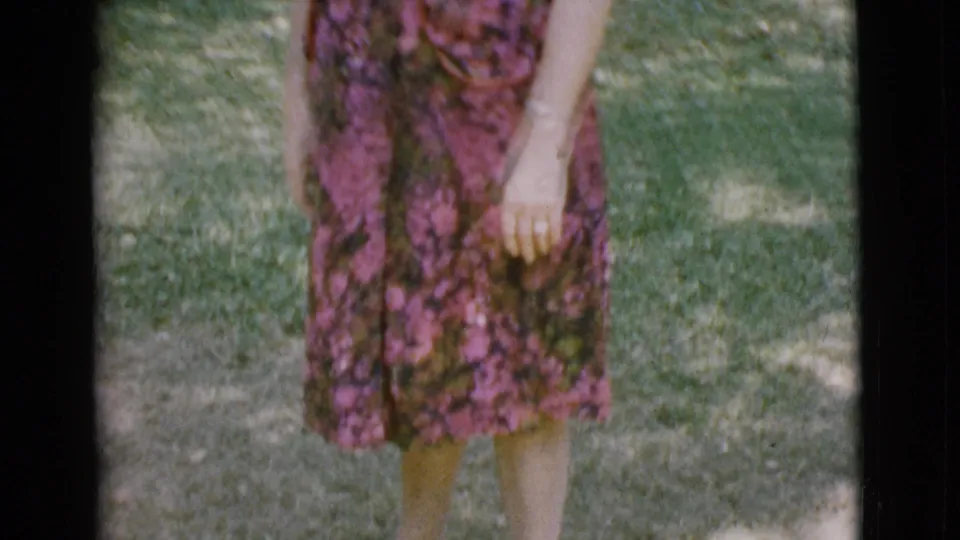 Adult woman in a rose floral dress stands on a grassy lawn in the Cottonwood, Arizona home-movie footage.