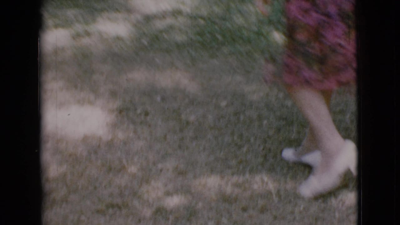 Woman's lower legs in white heels walking across a grassy lawn.