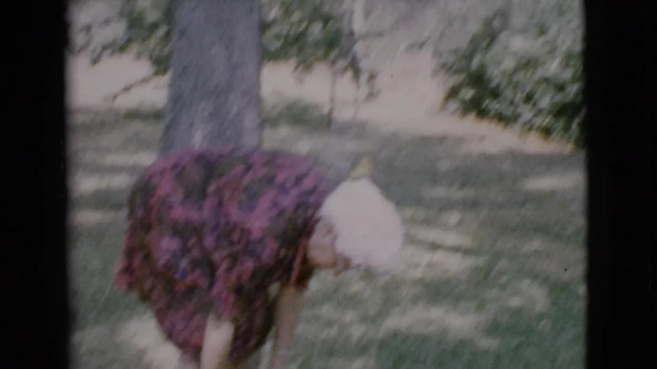 The woman bends forward in the Cottonwood backyard, reaching toward the ground near the puppy and a tree trunk.