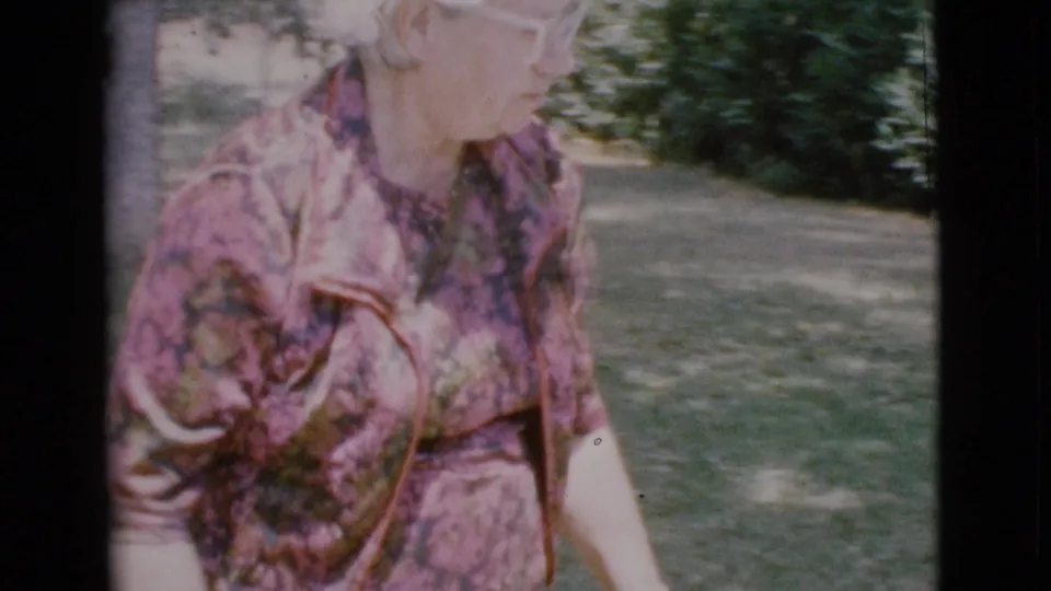 A closer 1968 8mm view shows the woman in a floral dress moving past lawn and shrubs, with her face partly visible at the frame edge.