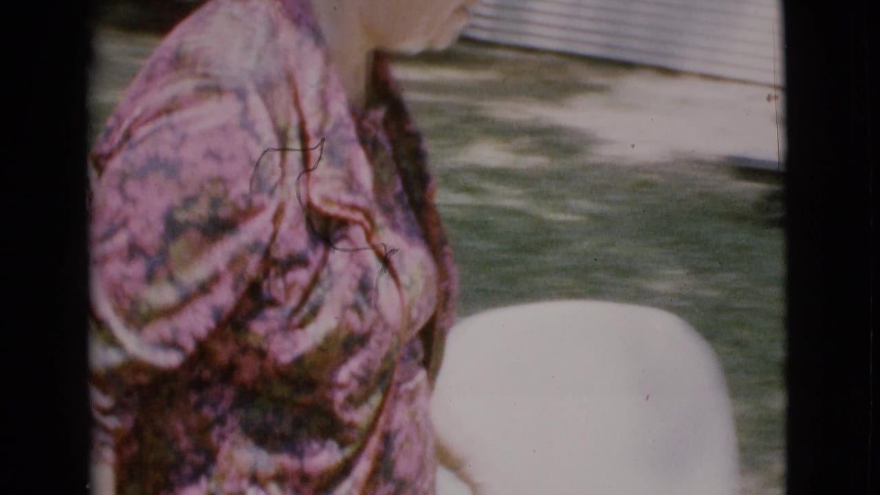 Elderly woman in a floral dress walking beside a grassy yard.