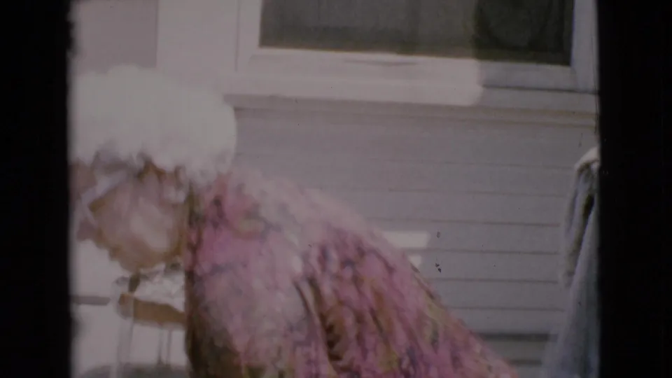 The woman leans forward near a white-sided house and window in Cottonwood, Arizona footage dated 1968.