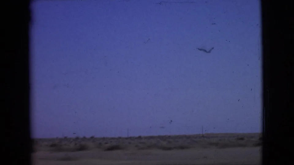 1968 San Diego County home-movie frame from inside a moving car, showing blue sky, low scrubland, and dark window edges.