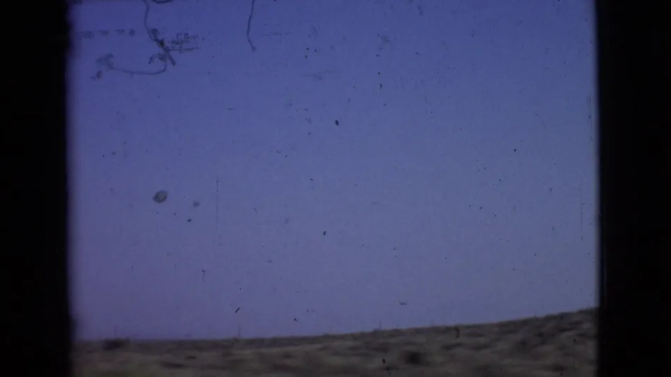1968 home-movie view from a moving car, with arid roadside vegetation, open sky, and dark vehicle-window borders.