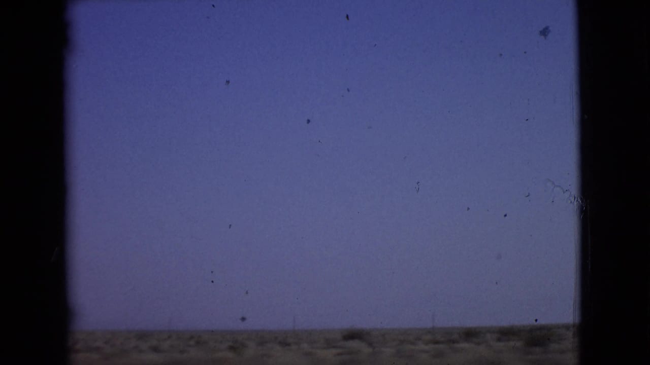 Blurred arid horizon and pale blue sky seen through dark car window edges.