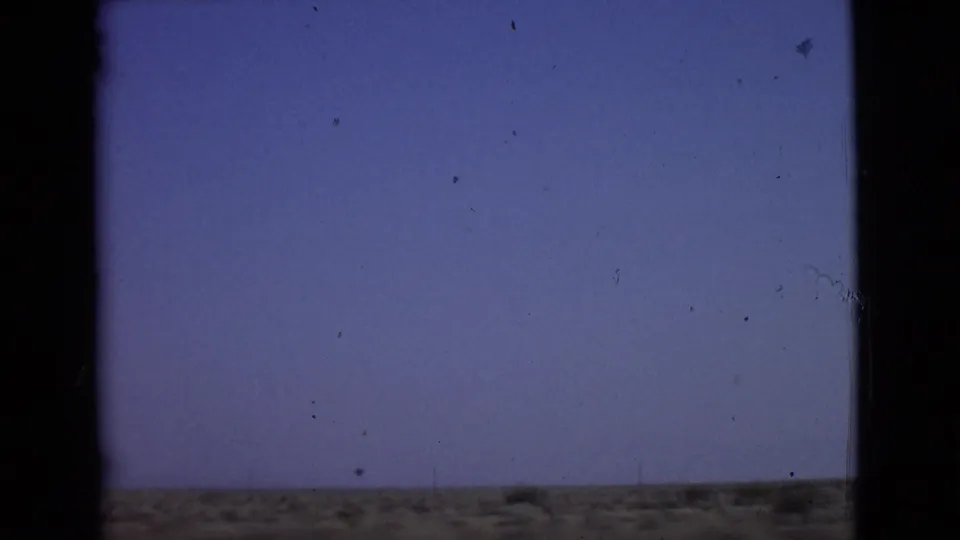 1968 8mm passenger view in San Diego County showing a low desert-like horizon, pale sky, and dark vertical car-window framing.