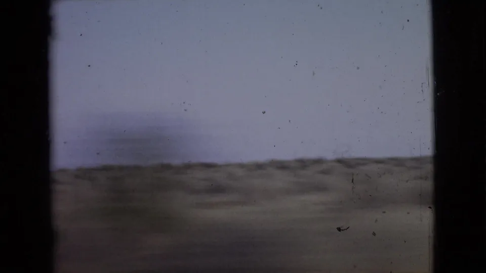 Passenger-side 8mm view of San Diego County terrain with a low scrub horizon, pale sky, and dark film or window borders.