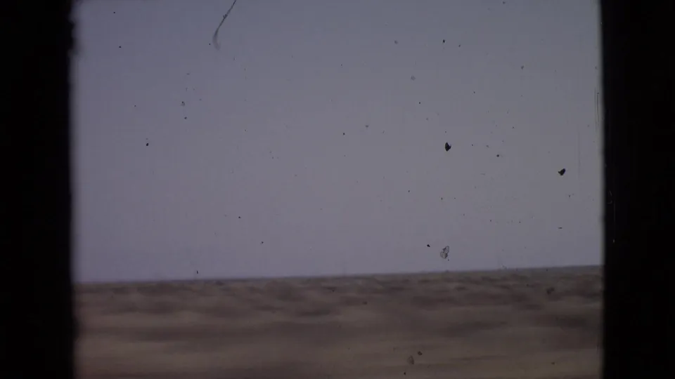 End frame from the 1968 8mm car-window sequence, with a pale sky, low arid horizon, and visible home-movie film texture.