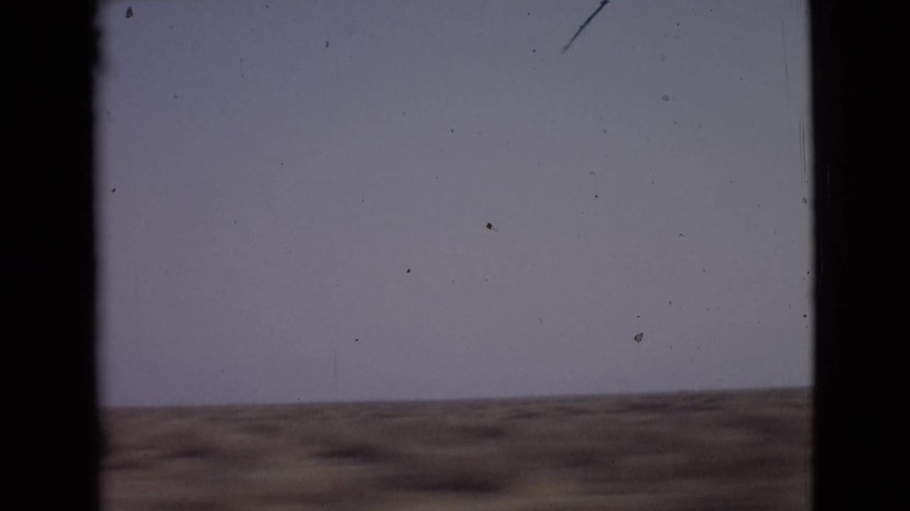 1968 8mm view of open San Diego County scrubland under a pale sky, framed by dark vertical film edges.