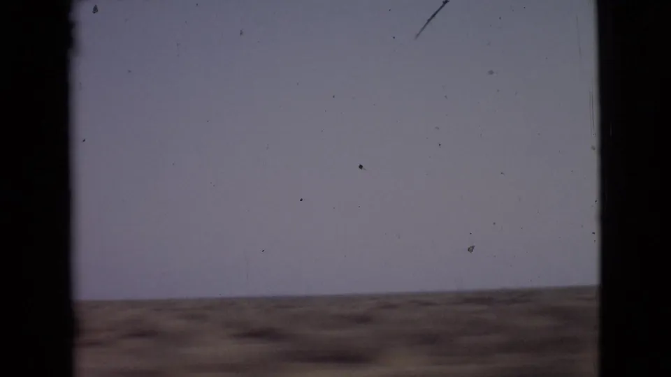 1968 8mm view of open San Diego County scrubland under a pale sky, framed by dark vertical film edges.