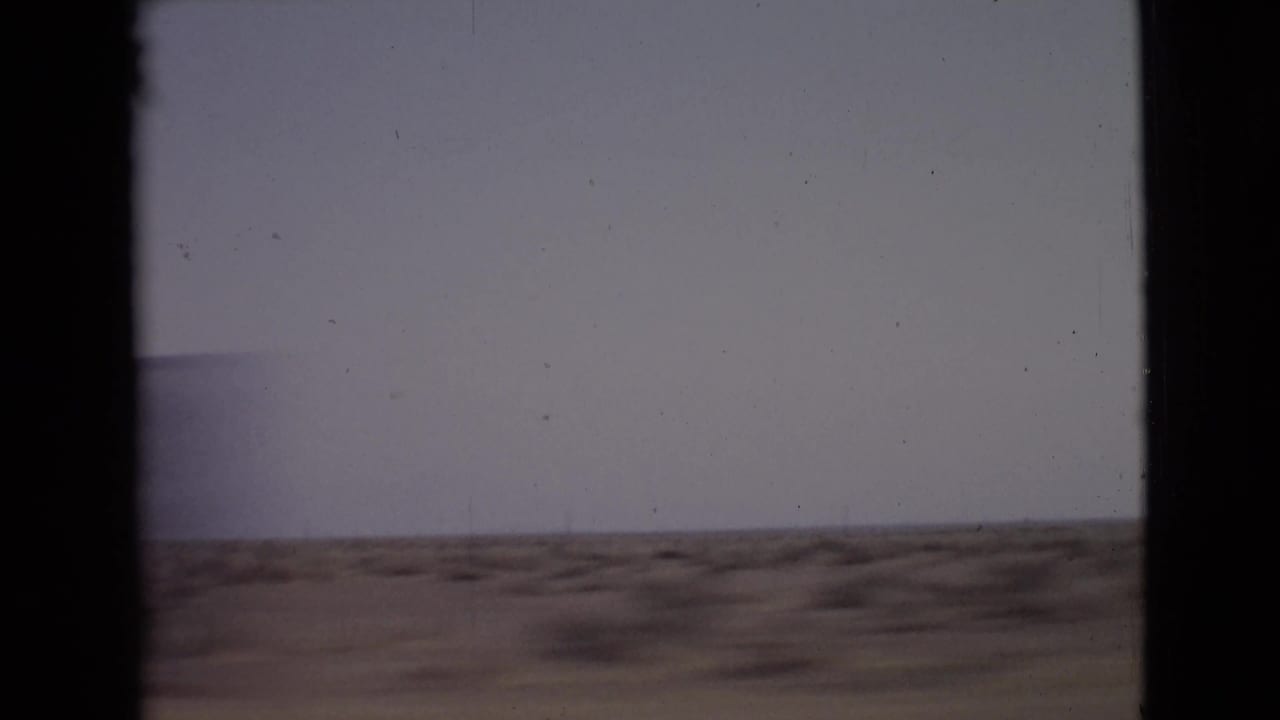 Flat arid ground with distant hills beneath a pale sky, divided by film borders.