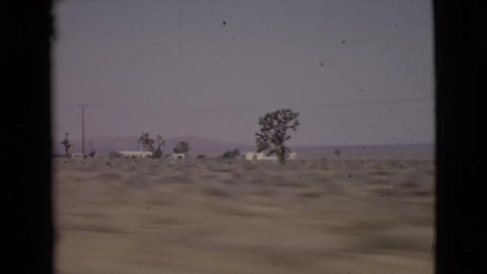 1968 San Diego County roadside view with small structures, a tree, utility lines, scrubland, and distant hills.