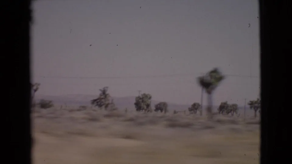 1968 San Diego County car-window view of sparse desert vegetation, utility lines, and a low mountain horizon.